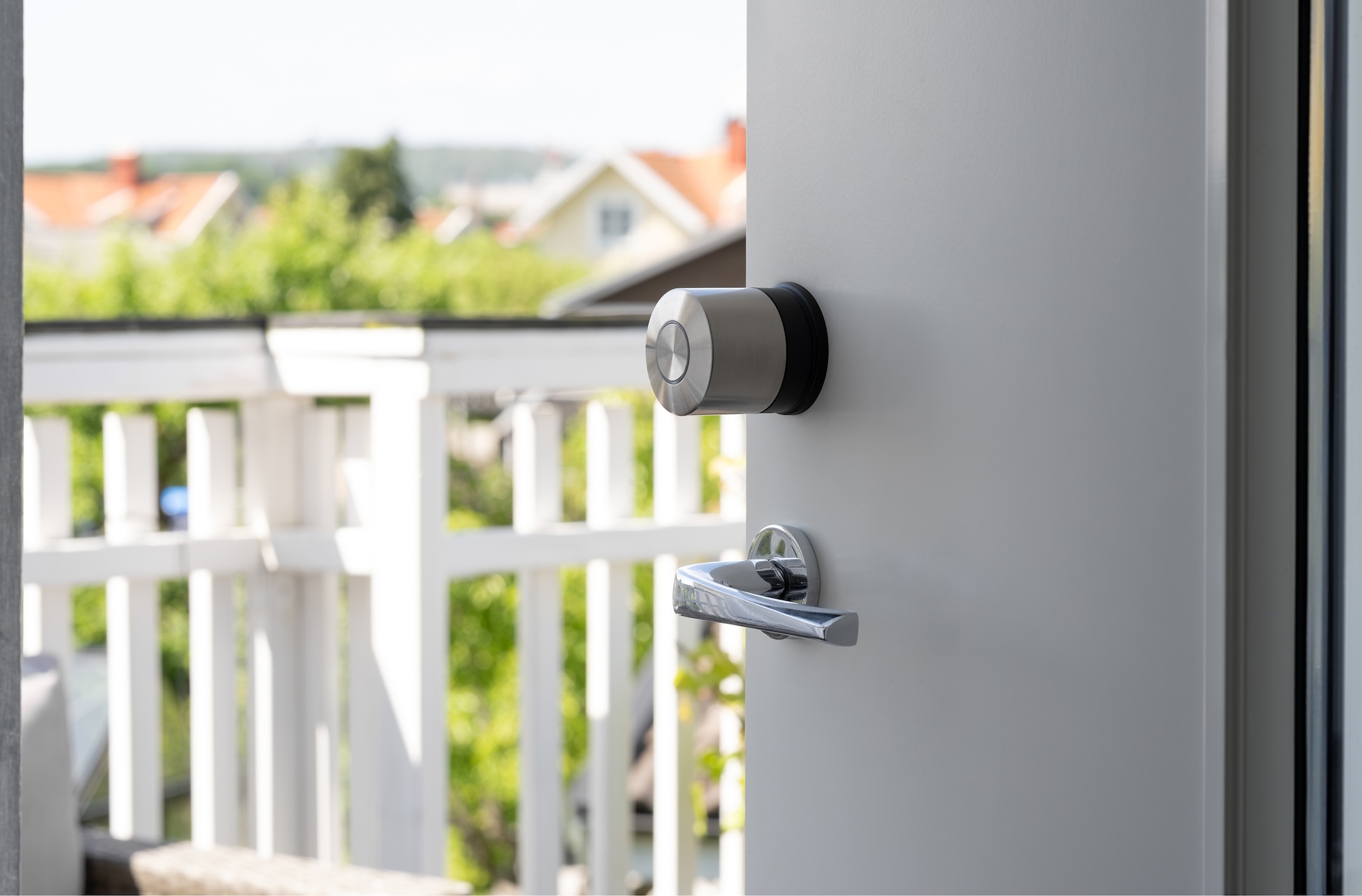 Smart Lock Ultra Nordics ist an einer Tür oberhalb des Türgriffs angebracht. Die Tür öffnet sich nach außen. Durch die offene Tür sind andere Häuser in einem nordischen Land zu sehen.